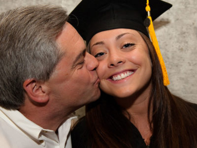 A dad kissing his graduate daughter.