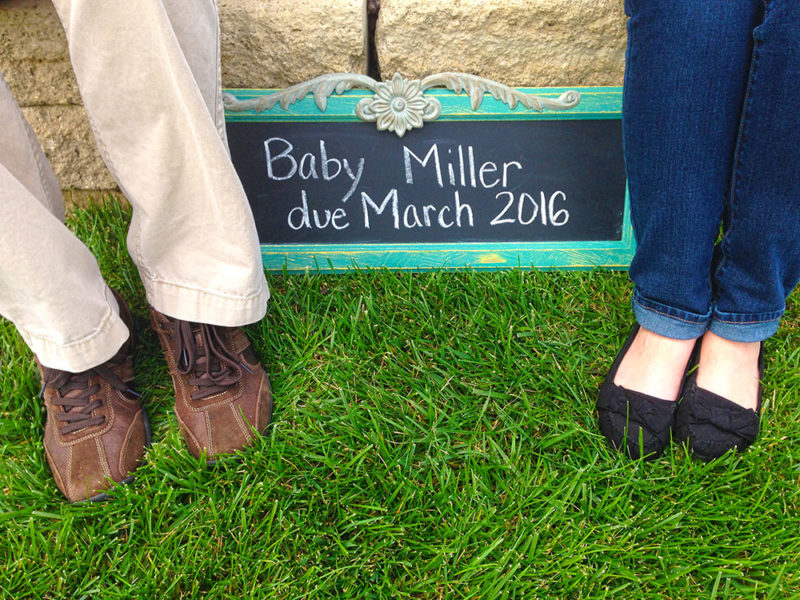 Chalk board with due date of Miller Baby, placed beside feet of parents.